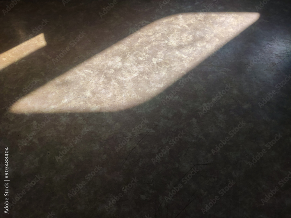 Abstract light and shadow reflections on a textured surface, creating geometric shapes with warm tones, contrast, and soft edges, evoking a minimalist, artistic, and moody atmosphere.