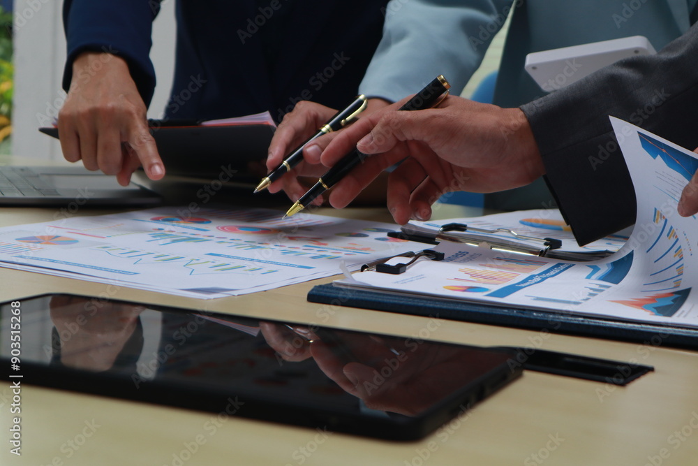 A businessman sits at a desk in an office, discussing documents with coworkers. Using a laptop, he engages in teamwork and communication, focusing on finance and corporate success A businessman sits at a desk in an office, discussing documents with coworkers. Using a laptop, he engages in teamwork and communication, focusing on finance and corporate success