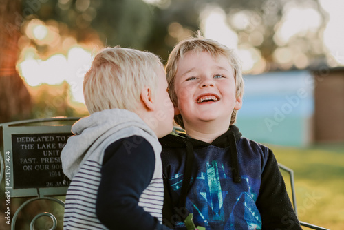 Two little boys sitting in garden setting at sunset telling secrets and laughing