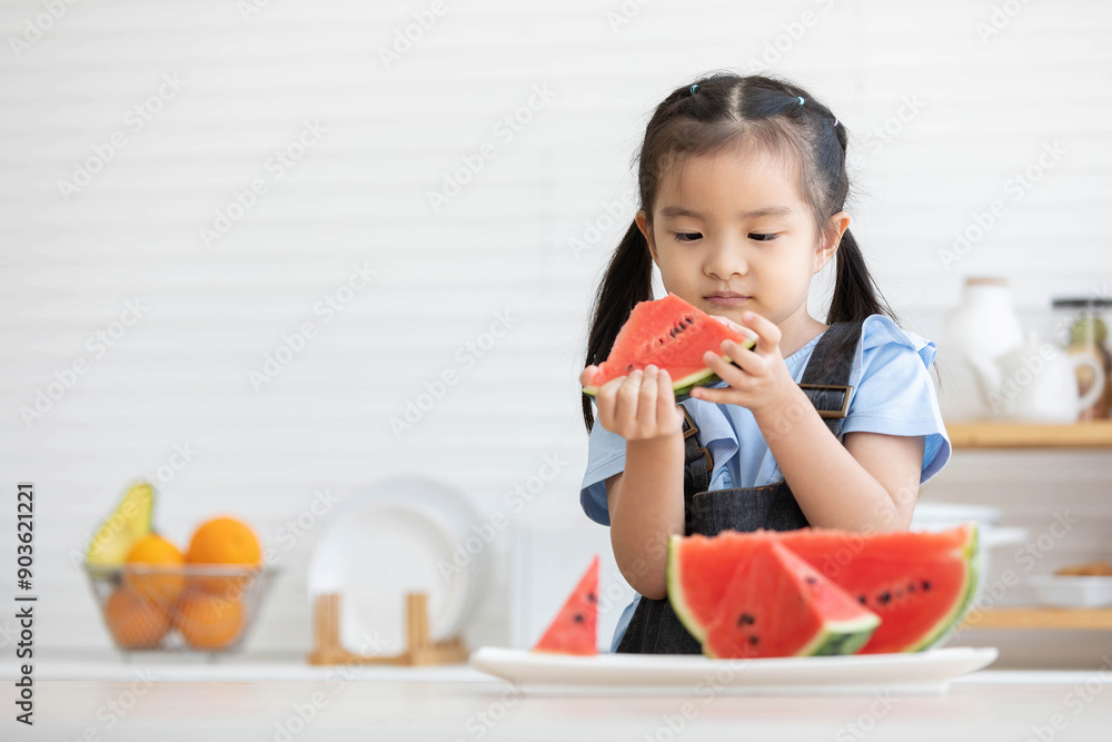 cute asian little child girl eating and looking slice watermelon in the kitchen
