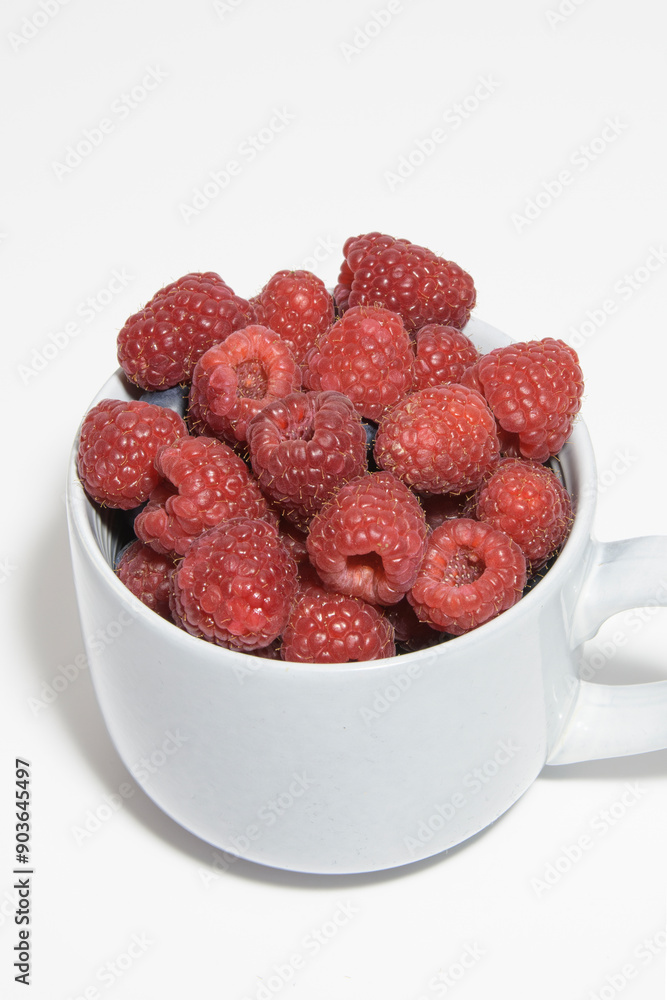Berries of ripe natural raspberries in a gray cup on a white table close-up Berries of ripe natural raspberries in a gray cup on a white table close-up