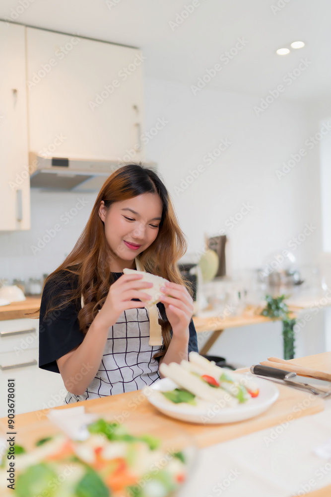Young asian woman enjoying to having breakfast with eating delicious sandwich while cooking fresh vegetables salad and homemade snack for health food in modern kitchen with healthy lifestyle in home Young asian woman enjoying to having breakfast with eating delicious sandwich while cooking fresh vegetables salad and homemade snack for health food in modern kitchen with healthy lifestyle in home