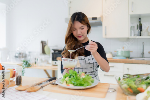 Young asian woman use spoon to adding mayonnaise into salad on plate while preparing fresh vegetables salad in bowl and cooking healthy breakfast food in modern kitchen with healthy lifestyle at home photo