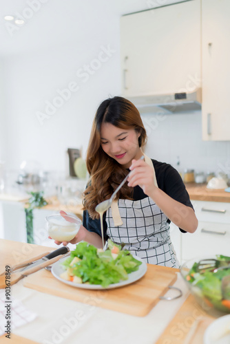 Young asian woman use spoon to adding mayonnaise into salad on plate while preparing fresh vegetables salad in bowl and cooking healthy breakfast food in modern kitchen with healthy lifestyle at home