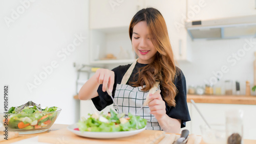 Young asian woman enjoying to eating vegetables salad after mixing fresh vegetables salad with dressing in bowl and cooking healthy breakfast food in modern kitchen with healthy lifestyle at home