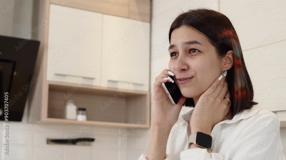 Young attractive woman in casual clothes standing in the cozy kitchen at home, talking with a friend on a smartphone and cheerfully smiling close up Young attractive woman in casual clothes standing in the cozy kitchen at home, talking with a friend on a smartphone and cheerfully smiling close up