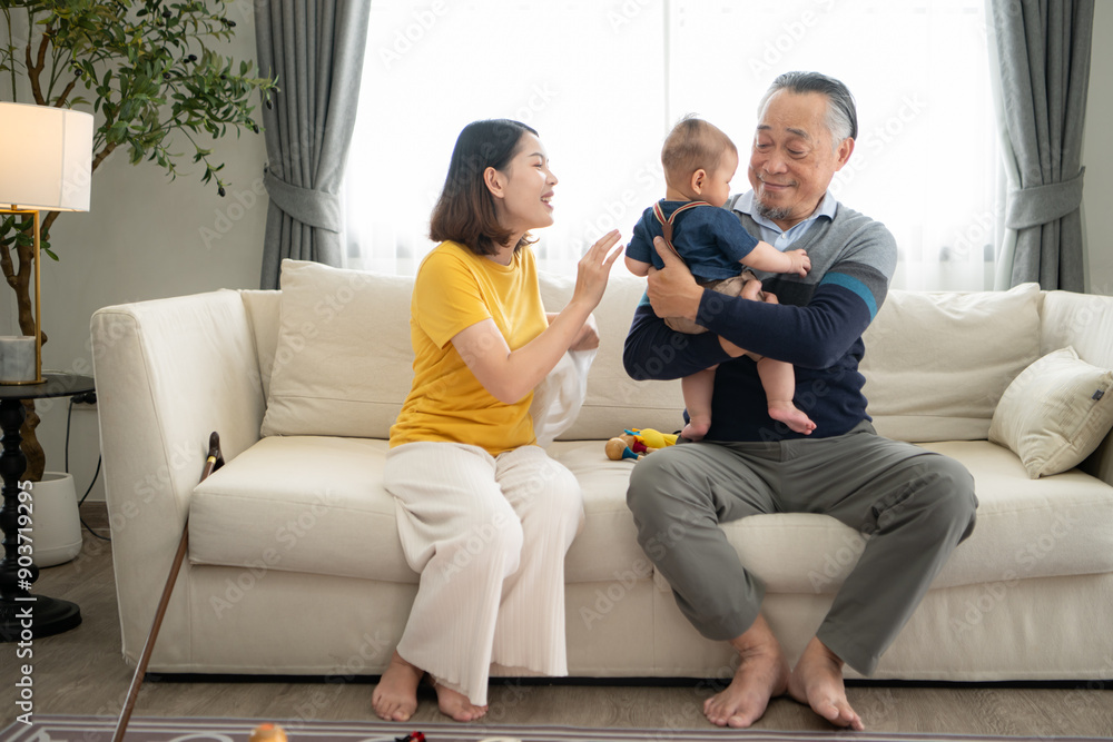 A tiny child smiling happily on the couch in the living room with mom and grandfather A tiny child smiling happily on the couch in the living room with mom and grandfather