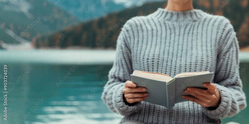 woman reading book in knit sweater by scenic lake in autumn with mountain background - peaceful relaxation and enjoying nature woman reading book in knit sweater by scenic lake in autumn with mountain background - peaceful relaxation and enjoying nature