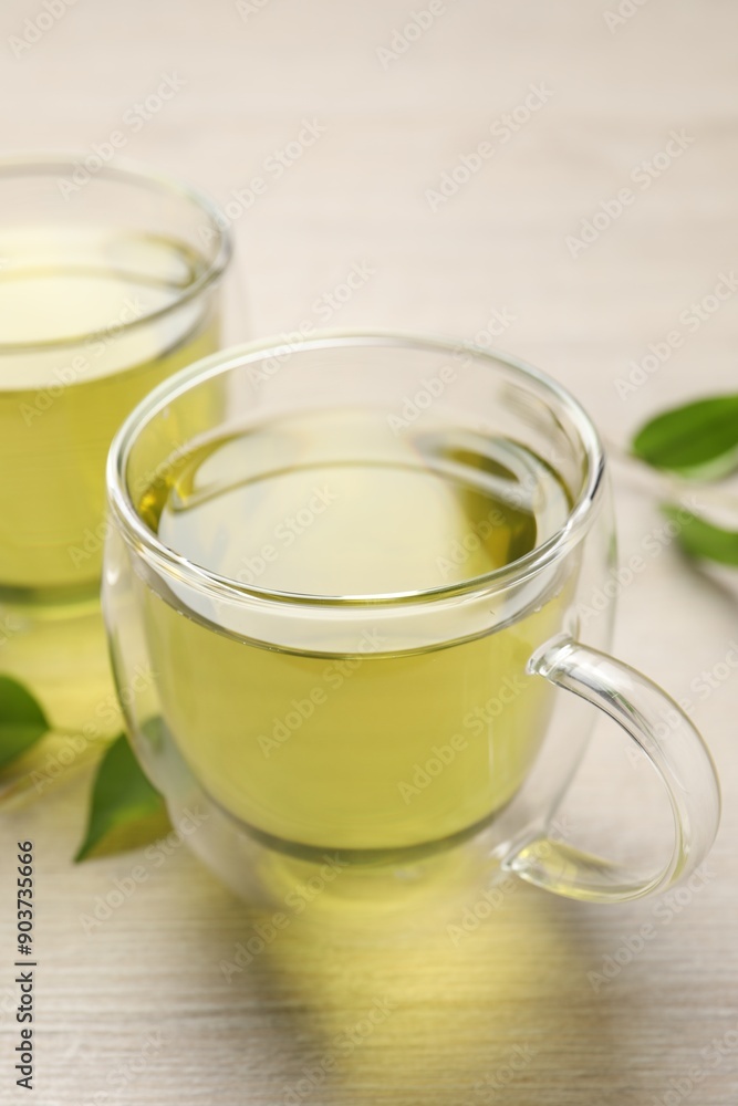 Refreshing green tea in cups and leaves on wooden table, closeup Refreshing green tea in cups and leaves on wooden table, closeup
