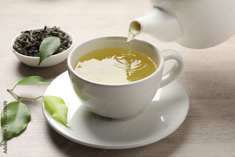 Pouring refreshing green tea into cup at wooden table, closeup Pouring refreshing green tea into cup at wooden table, closeup