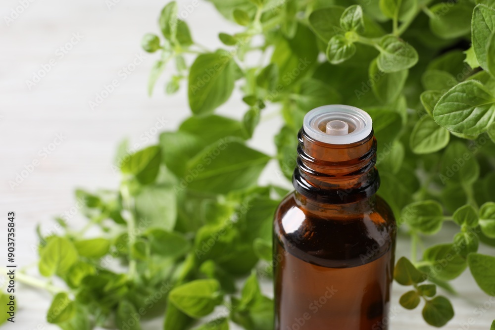 Essential oil in bottle and oregano leaves on white background, closeup. Space for text Essential oil in bottle and oregano leaves on white background, closeup. Space for text