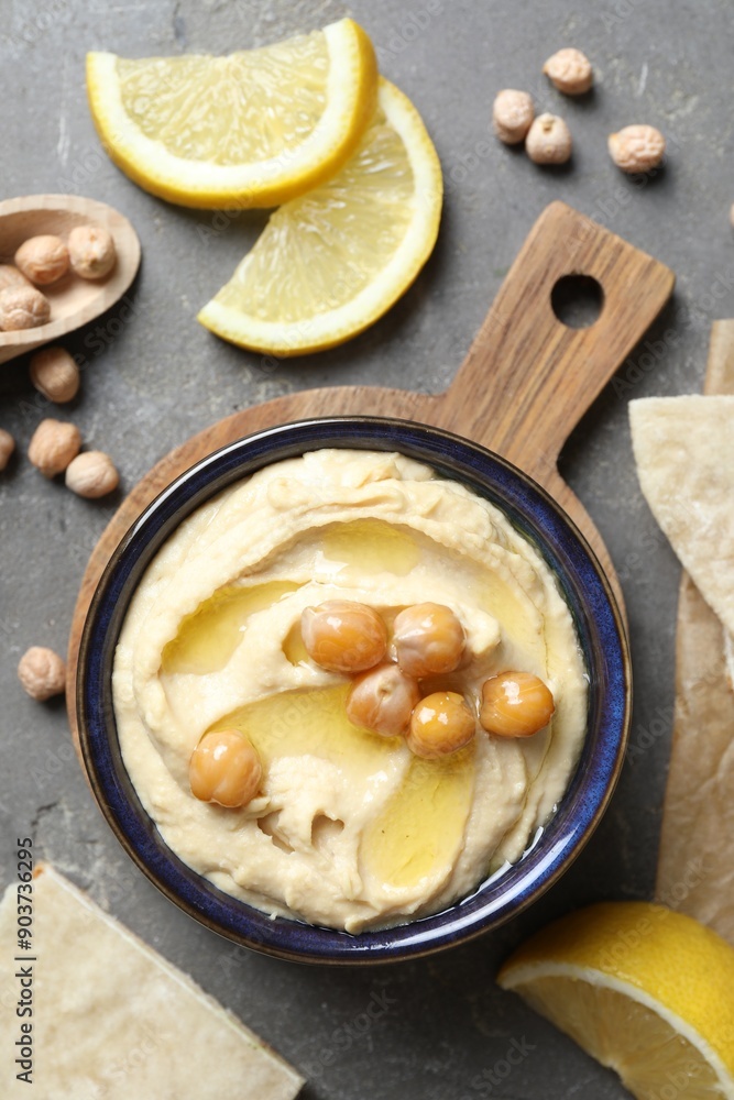 Delicious hummus with olive oil, chickpeas, lemon and pita on grey textured table, flat lay Delicious hummus with olive oil, chickpeas, lemon and pita on grey textured table, flat lay