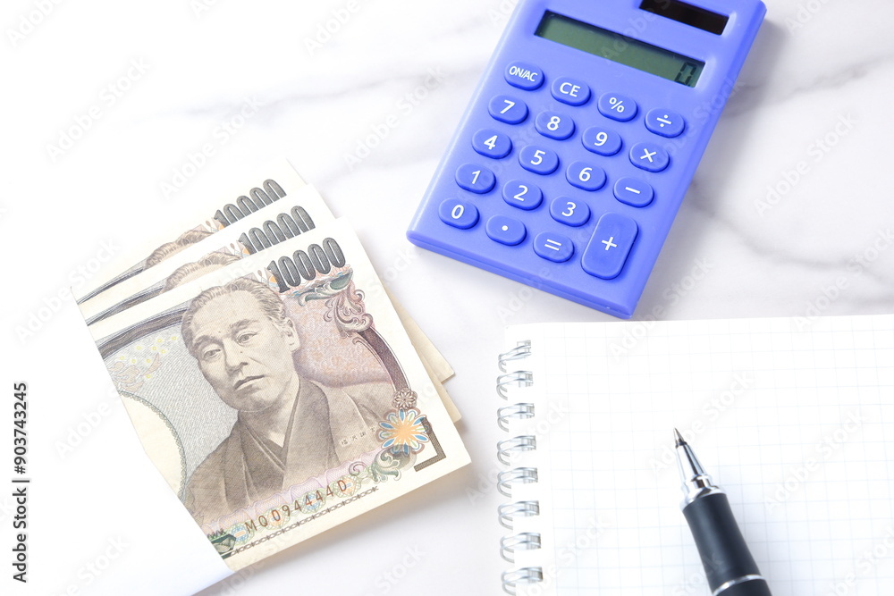 福沢諭吉の肖像の一万円紙幣と電卓、メモ帳とペン
福沢諭吉の肖像の一万円紙幣と電卓、メモ帳とペン