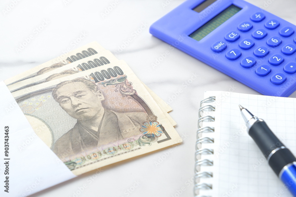 福沢諭吉の肖像の一万円紙幣と電卓、メモ帳とペン
福沢諭吉の肖像の一万円紙幣と電卓、メモ帳とペン
