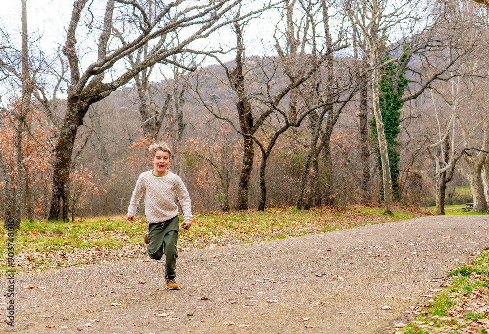 Caucasian boy running with funny face looking at camera in a park in autumn Caucasian boy running with funny face looking at camera in a park in autumn