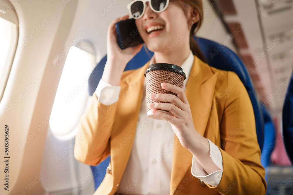 Naklejka premium An Asian businesswoman travels abroad by plane, sitting near the window. She reads a book and uses her computer, utilizing her airline credit card to manage travel expenses efficiently.