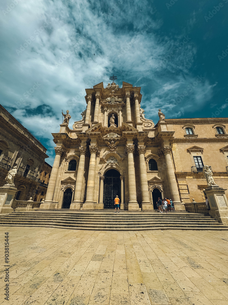 Obraz premium A large church with a clock tower and a cross on top. The building is surrounded by a courtyard