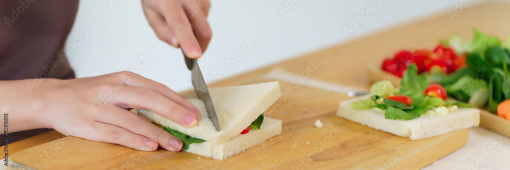 Asian women making delicious sandwich with vegetables and mayonnaise to cutting sandwich with knife on cutting board while cooking breakfast meal and making healthy food lifestyle in kitchen at home Asian women making delicious sandwich with vegetables and mayonnaise to cutting sandwich with knife on cutting board while cooking breakfast meal and making healthy food lifestyle in kitchen at home