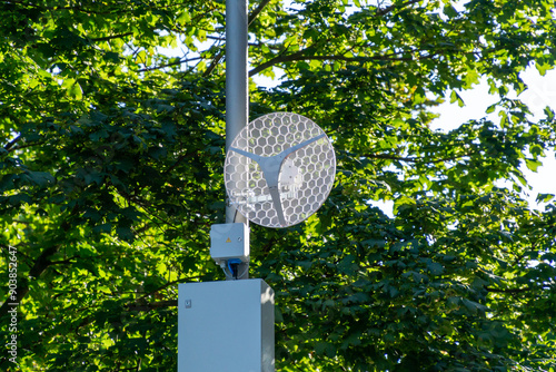 Wireless antenna on a street light pole with an electric box, green trees in the background