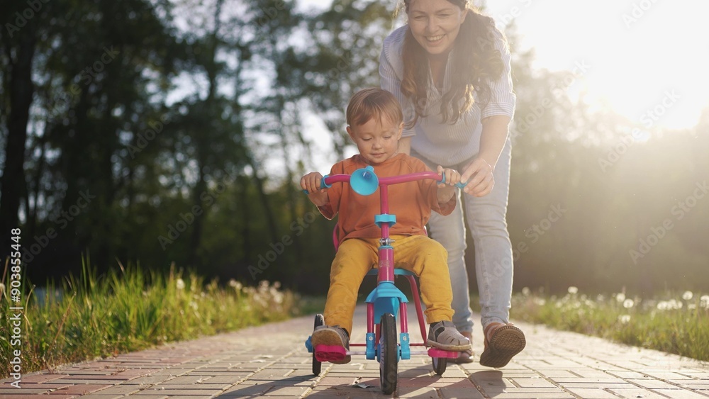 The boy kid riding his bike. happy family a kid dream concept. Mom teaches son bike. child rides a bike in the park in the summer, mother helps teaches, plays lifestyle with son The boy kid riding his bike. happy family a kid dream concept. Mom teaches son bike. child rides a bike in the park in the summer, mother helps teaches, plays lifestyle with son