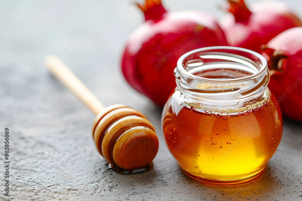A festive scene for Rosh Hashanah with honey jar, honey dipper and red pomegranates on a gray background, designed for banners with copy space. A festive scene for Rosh Hashanah with honey jar, honey dipper and red pomegranates on a gray background, designed for banners with copy space.