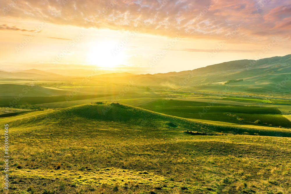 Fototapeta premium spring green field landscape in beautiful countryside with green and yellow grass, rural hills and amazing cloudy sky on background. Agriculture landscape with rural view