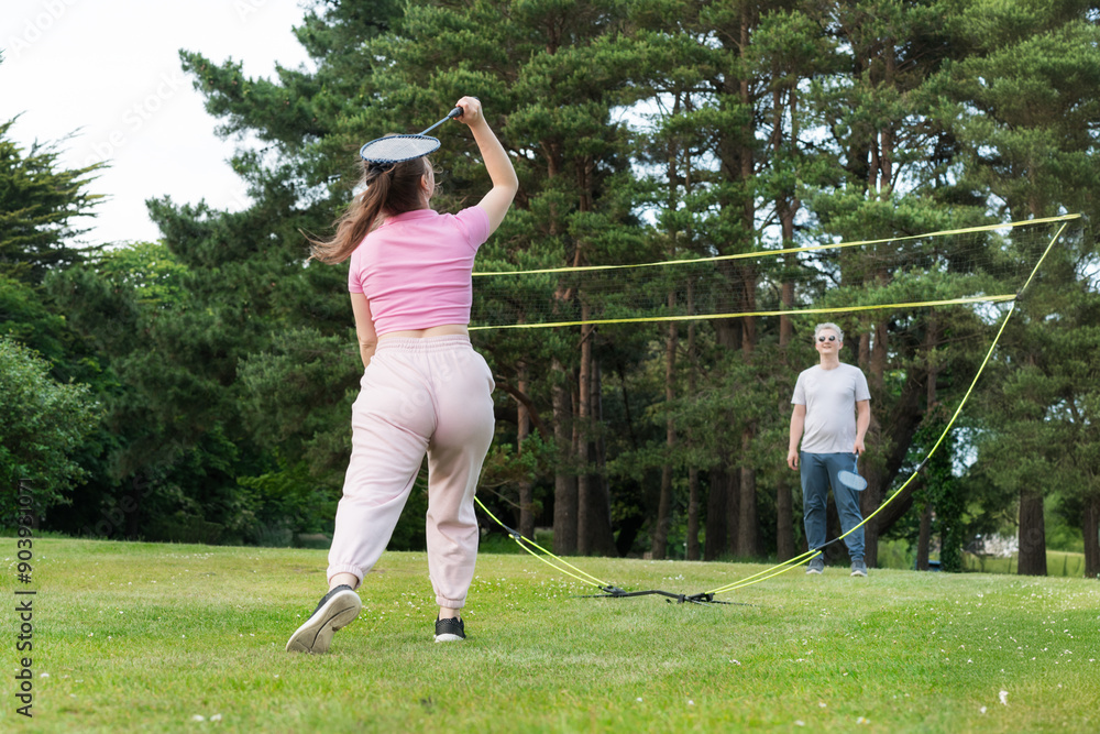 Focus on young woman with racket playing badminton with man in the park. Friends having fun and training outdoors. Enjoying game and natural environment. Adult Outdoor activity. Healthy lifestyle. Focus on young woman with racket playing badminton with man in the park. Friends having fun and training outdoors. Enjoying game and natural environment. Adult Outdoor activity. Healthy lifestyle.
