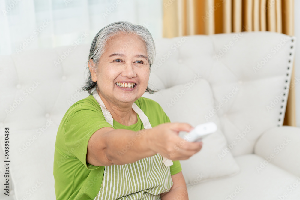 Asian senior woman with air conditioner remote control in living room, Woman switching on air conditioning Asian senior woman with air conditioner remote control in living room, Woman switching on air conditioning