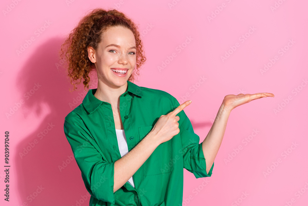 Photo of charming positive woman wear green shirt holding arm pointing finger empty space isolated pink color background Photo of charming positive woman wear green shirt holding arm pointing finger empty space isolated pink color background