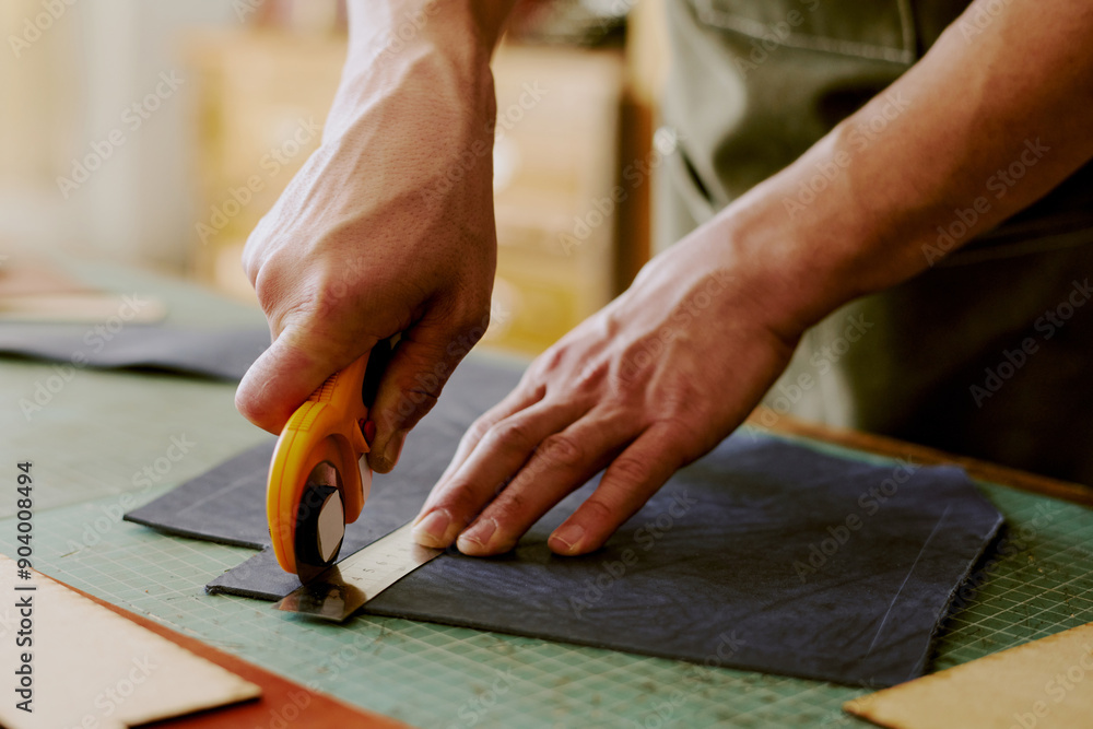 Unrecognizable male hands holding round knife and steel ruler to cut out deep blue leather workpieces Unrecognizable male hands holding round knife and steel ruler to cut out deep blue leather workpieces