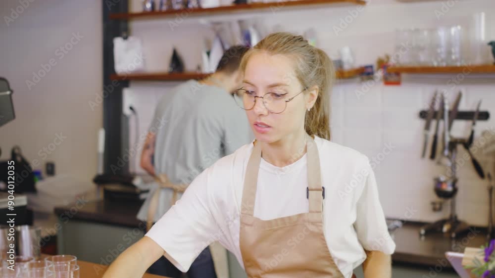 In a cozy and friendly cafe, a young barista girl is wiping down the countertop while a barista guy prepares the coffee machine. The warm and inviting atmosphere of the cafe reflects their dedication In a cozy and friendly cafe, a young barista girl is wiping down the countertop while a barista guy prepares the coffee machine. The warm and inviting atmosphere of the cafe reflects their dedication