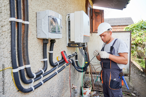 Man electrician installing solar panel system. Technician in helmet and gloves making electrical wiring inverter and electric box. Concept of alternative and renewable energy.