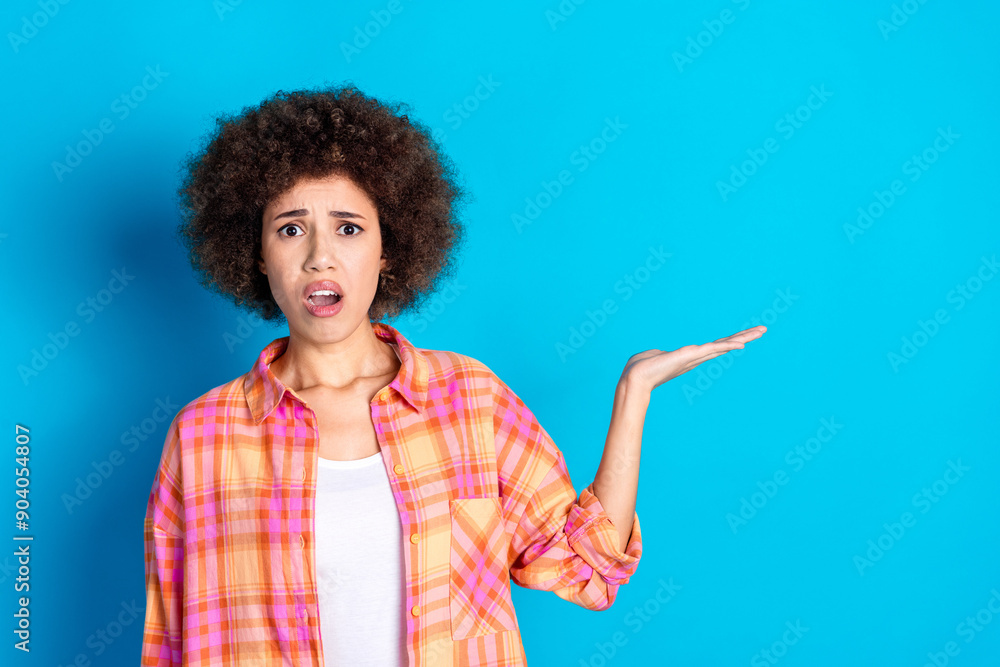 Photo portrait of lovely young lady hold frightened empty space dressed stylish checkered garment isolated on blue color background Photo portrait of lovely young lady hold frightened empty space dressed stylish checkered garment isolated on blue color background