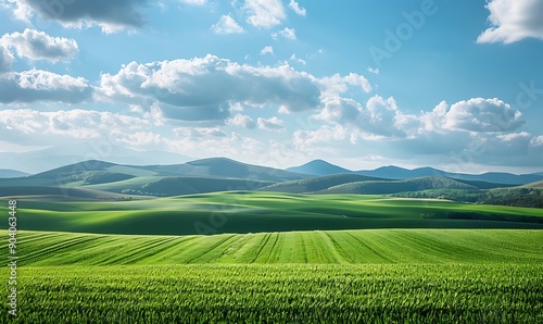 Rolling green fields extending to the horizon, with picturesque mountains and a sky filled with beautiful, textured clouds