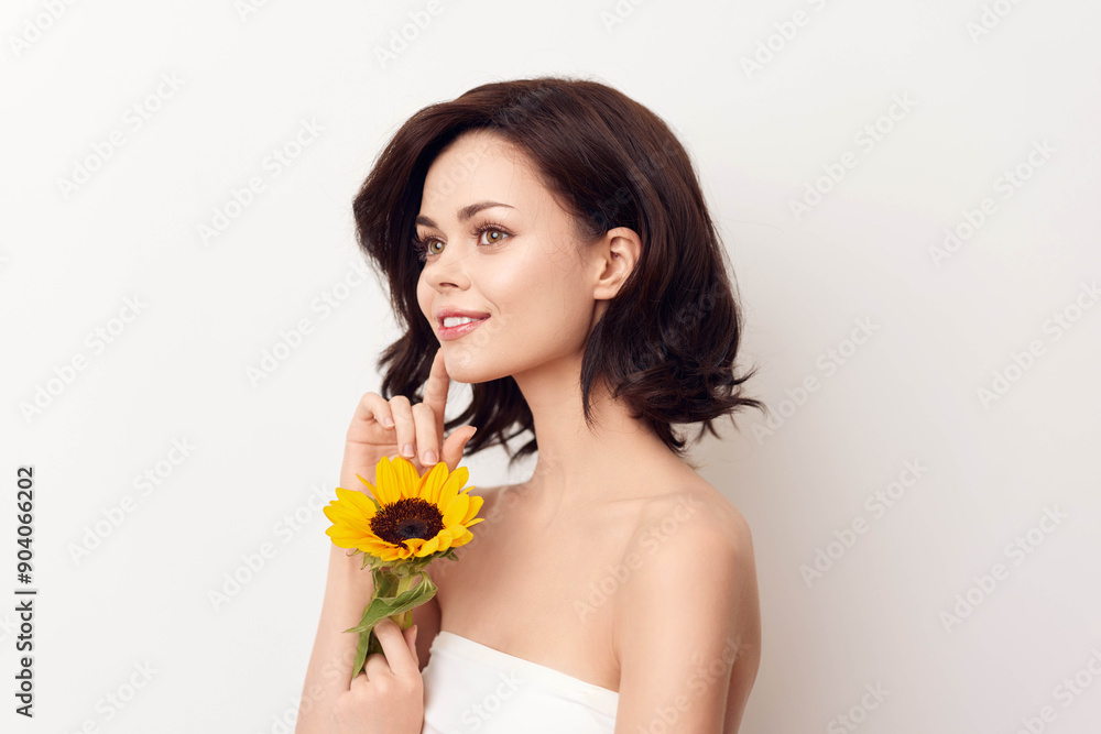 Young woman in white dress holding sunflower and looking at the camera on a white background Young woman in white dress holding sunflower and looking at the camera on a white background
