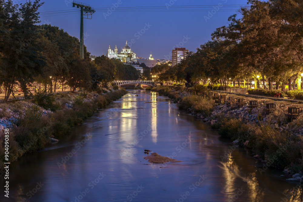 Fototapeta premium Panoramic view of Madrid at night, during the blue hour, with the Almudena cathedral in the background, over the Reina Victoria bridge, which crosses the Manzanares river.