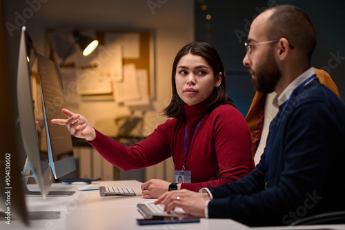 Portrait of computer development team discussing project in office with young woman pointing at screen