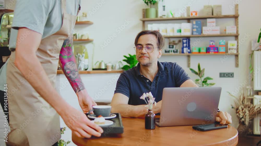 In a modern and cozy cafe, a man is seated at a table with his laptop open, working intently. A barista guy approaches and delivers a freshly brewed coffee, enhancing the comfortable and productive In a modern and cozy cafe, a man is seated at a table with his laptop open, working intently. A barista guy approaches and delivers a freshly brewed coffee, enhancing the comfortable and productive