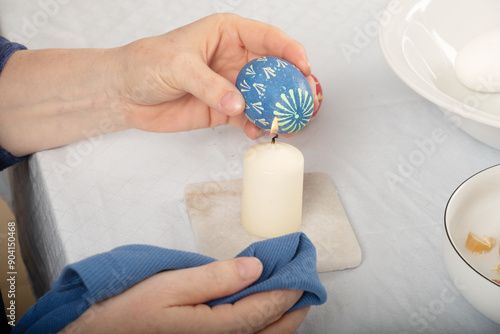 sorbian Woman's hands remove with a candle flame the wax according to Sorbian tradition of the blue colored Easter egg photo