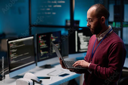 Fotografija Side view portrait of bearded adult man as computer programmer holding open lapt
