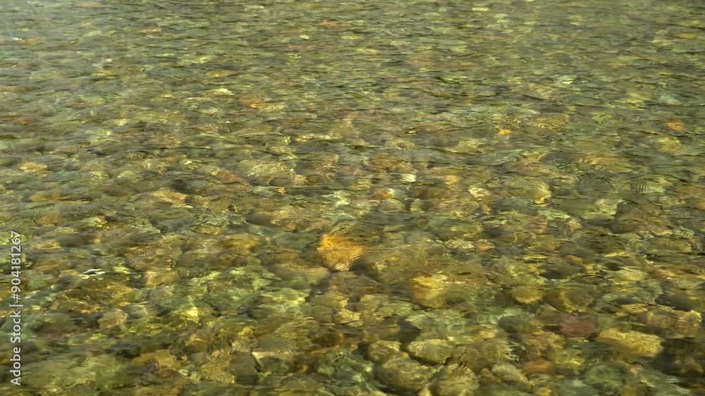 The rocky bottom is visible through the ripples of the water The rocky bottom is visible through the ripples of the water