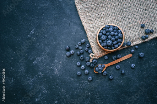 Photos Wooden bowl filled with fresh blueberries and a wooden spoon with a few berries on a dark surface