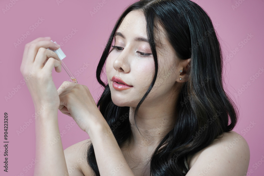 Fototapeta premium Beautiful Asian woman with Korean style makeup holding a bottle of perfume smelling the fragrance on a pink background