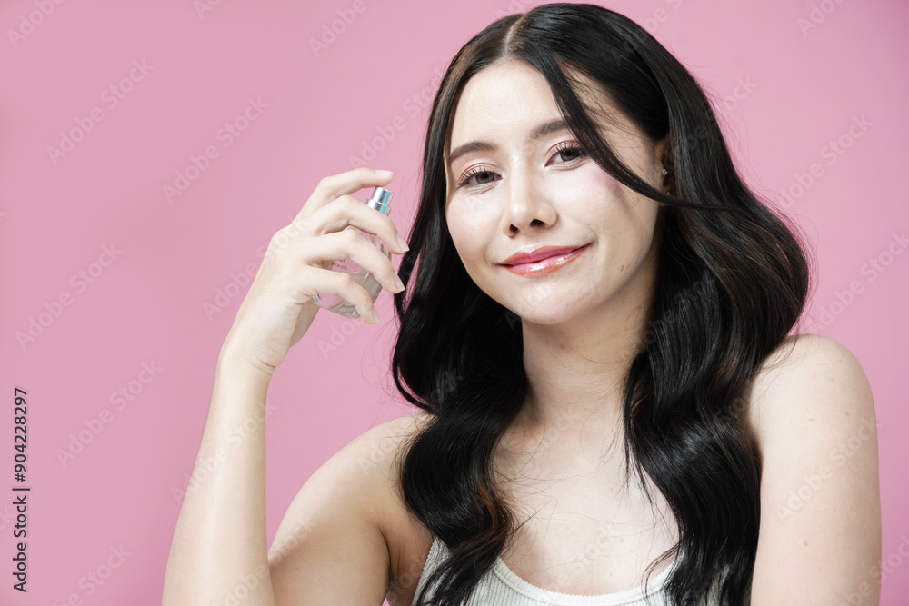 Beautiful Asian woman with Korean style makeup holding a bottle of perfume smelling the fragrance on a pink background Beautiful Asian woman with Korean style makeup holding a bottle of perfume smelling the fragrance on a pink background