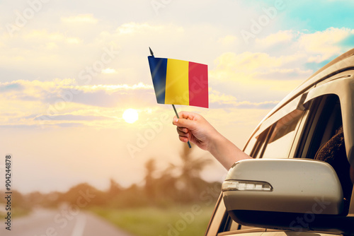 Waving the Romania flag against the sunrise or sunset from a car driving along a country road. Holding the Romania flag, traveling by car, on a weekend trip.