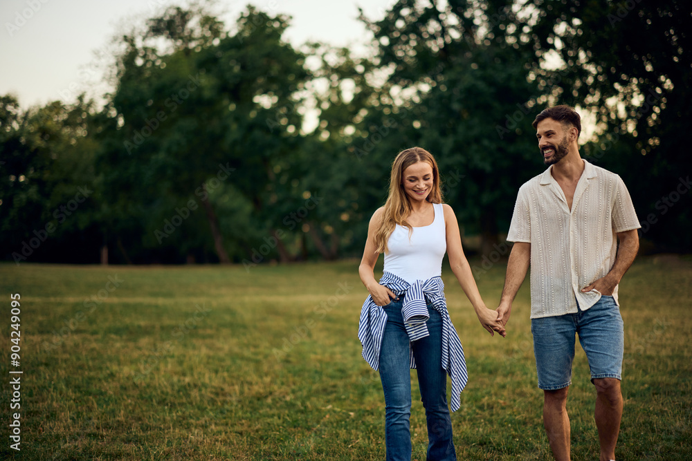 A smiling couple walking and talking through the park, holding hands. A smiling couple walking and talking through the park, holding hands.