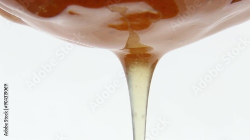 An incessant stream of liquid, fresh honey flows slowly against a white background. Natural, sweet beekeeping food. Honey syrup. Macro. Asmr.