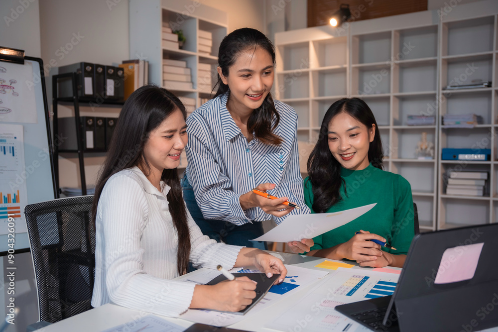 Three young businesswomen smiling and working together, discussing financial data and using a laptop in a modern office Three young businesswomen smiling and working together, discussing financial data and using a laptop in a modern office
