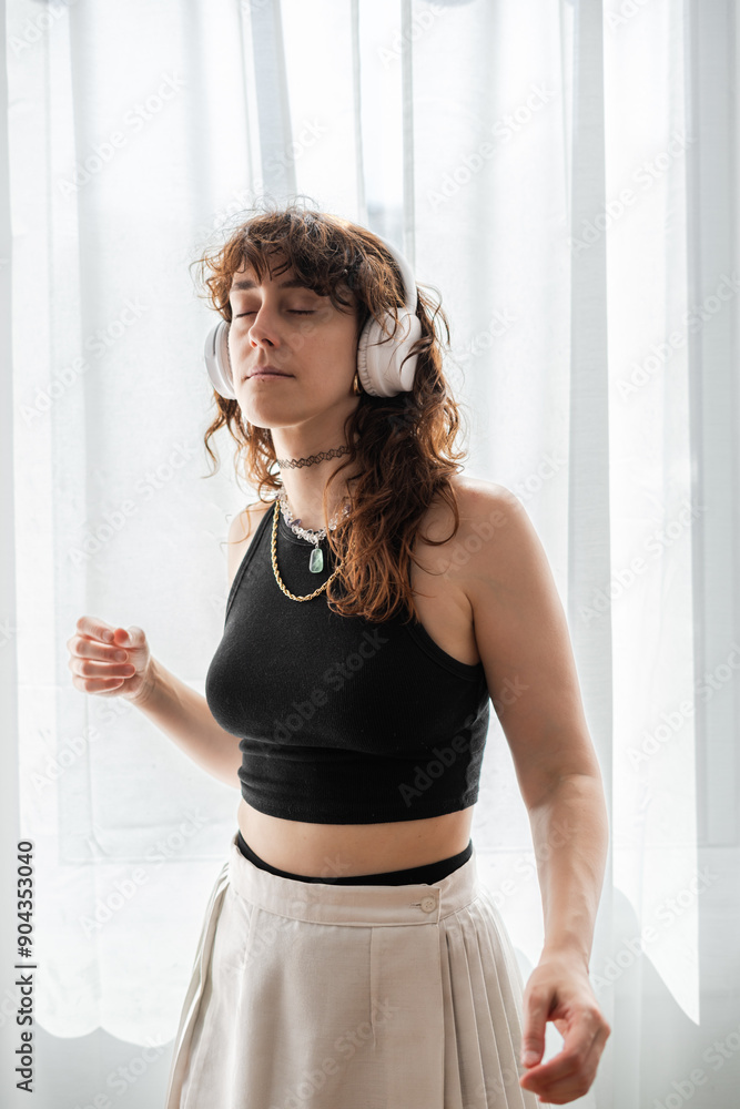 woman dances in front of the window while listening to music on her headphones woman dances in front of the window while listening to music on her headphones