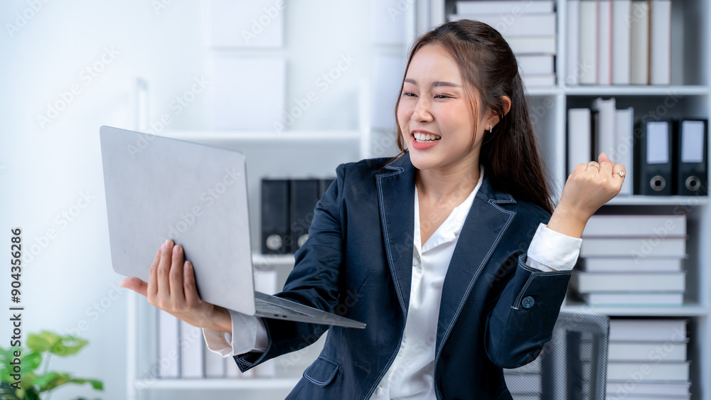 Asian businesswoman smiling happily while working on laptop at table in office Asian businesswoman smiling happily while working on laptop at table in office